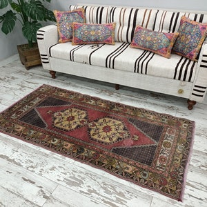 May include: A pink and cream patterned rug with a dark brown center. The rug has a traditional design with floral motifs and geometric shapes. The rug is laid out on a whitewashed wood floor.