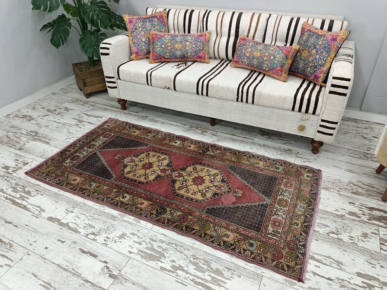 May include: A pink and cream patterned rug with a dark brown center. The rug has a traditional design with floral motifs and geometric shapes. The rug is laid out on a whitewashed wood floor.