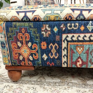 May include: A blue and orange patterned storage ottoman with wooden legs. The ottoman has a hinged lid and is made of fabric.
