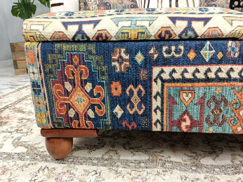May include: A blue and orange patterned storage ottoman with wooden legs. The ottoman has a hinged lid and is made of fabric.