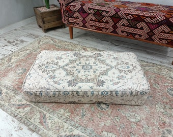 May include: A white and beige patterned floor cushion with a geometric design. The cushion is sitting on a rug with a similar pattern.