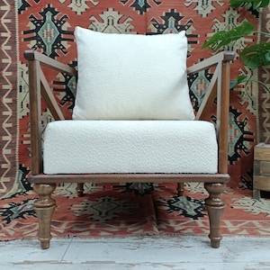 May include: A white armchair with a white cushion and wooden legs. The chair is in front of a red and black patterned rug.