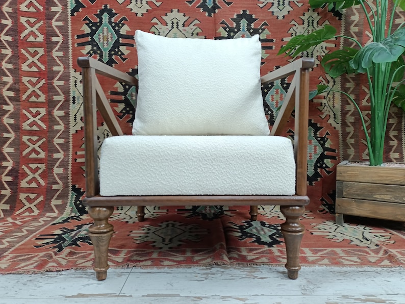 May include: A white armchair with a white cushion and wooden legs. The chair is in front of a red and black patterned rug.