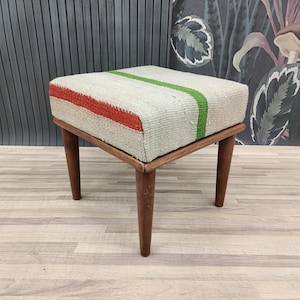 May include: A small, rectangular stool with a wooden frame and a woven fabric seat. The fabric is white with green and red stripes.