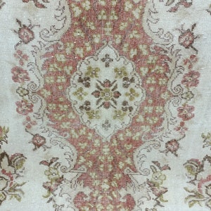 Op de afbeelding: Een vintage tapijt met een bloemenpatroon in tinten bruin, rood en wit. Het tapijt heeft een centraal medaillon met een herhalend patroon van bloemen en bladeren.