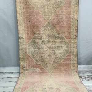 May include: A vintage rug with a faded pink and green colour scheme. The rug has a central diamond-shaped design with intricate floral patterns. The rug is worn and has a distressed look.