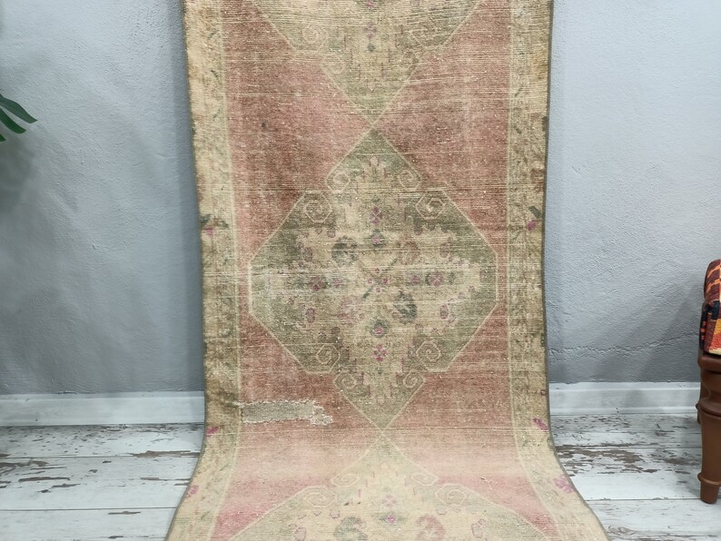 May include: A vintage rug with a faded pink and green colour scheme. The rug has a central diamond-shaped design with intricate floral patterns. The rug is worn and has a distressed look.