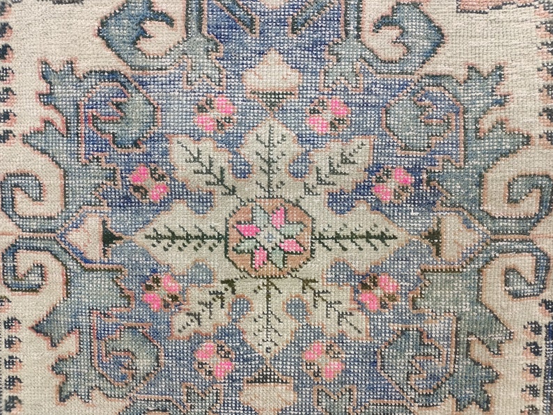 Pode incluir: Close-up de um tapete vintage com um padr&atilde;o floral azul e branco. O tapete tem um medalh&atilde;o central com um design rosa e verde. O tapete &eacute; tecido com grande detalhe.