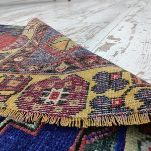 May include: A colorful, hand-woven rug with intricate patterns in shades of red, yellow, blue, and green. The rug has a fringed edge and is folded in half.