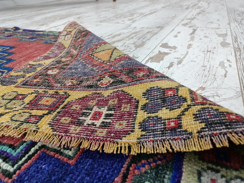 May include: A colorful, hand-woven rug with intricate patterns in shades of red, yellow, blue, and green. The rug has a fringed edge and is folded in half.
