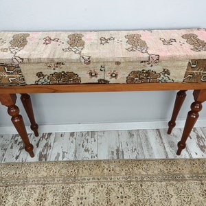 Op de afbeelding: Een houten consoletafel met een gepatroneerd stoffen blad. De tafel heeft vier gedraaide poten en een rechthoekig blad. De stof is een patchwork van verschillende patronen in tinten bruin, roze en wit.