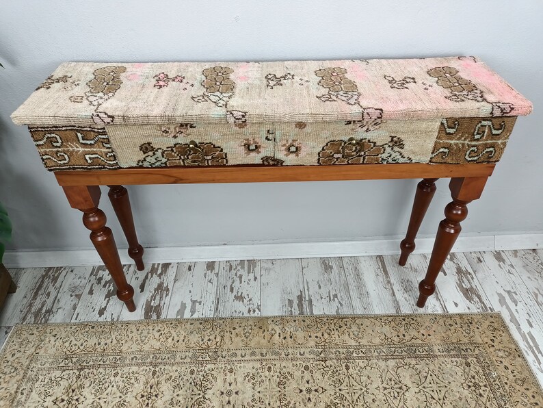 Op de afbeelding: Een houten consoletafel met een gepatroneerd stoffen blad. De tafel heeft vier gedraaide poten en een rechthoekig blad. De stof is een patchwork van verschillende patronen in tinten bruin, roze en wit.