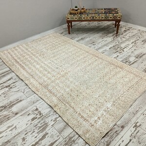 Puede incluir: Una alfombra vintage blanca y crema con un patr&oacute;n floral y un borde. La alfombra est&aacute; colocada sobre un suelo de madera blanqueada.