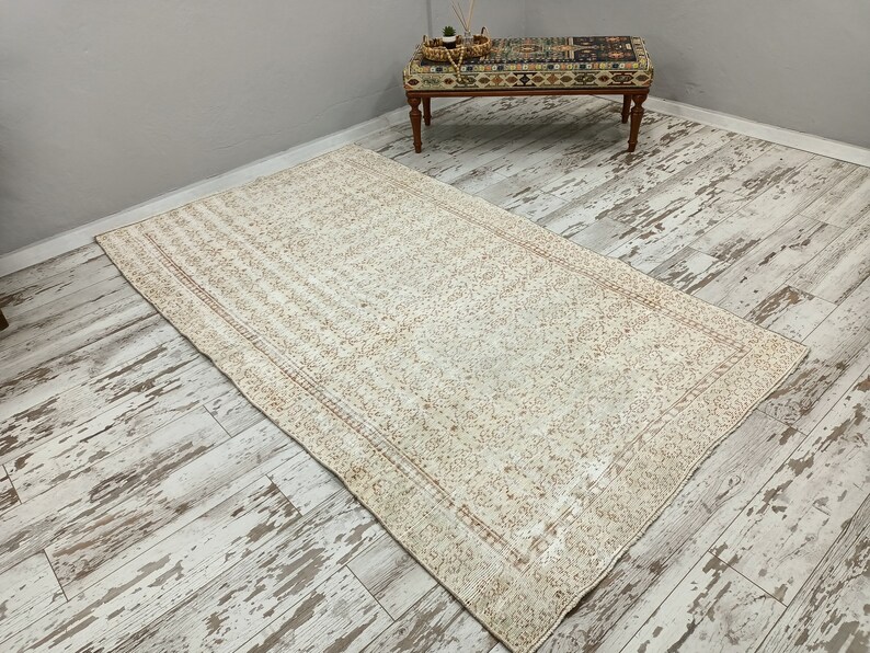 Puede incluir: Una alfombra vintage blanca y crema con un patr&oacute;n floral y un borde. La alfombra est&aacute; colocada sobre un suelo de madera blanqueada.