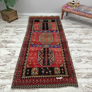 May include: A red, black, and blue patterned runner rug with a geometric design. The rug has a fringe border and is approximately 2.5 feet wide and 8 feet long.
