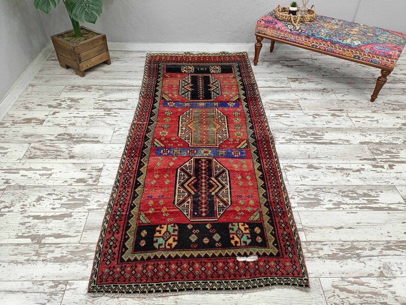 May include: A red, black, and blue patterned runner rug with a geometric design. The rug has a fringe border and is approximately 2.5 feet wide and 8 feet long.