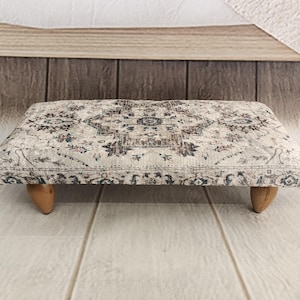 A decorative ottoman with a patterned fabric sits on a wooden floor against a wooden wall.
