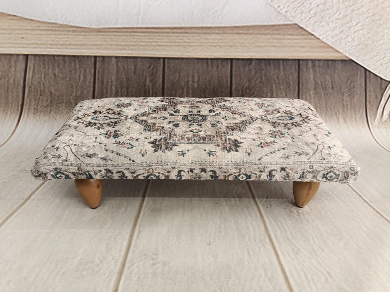 A decorative ottoman with a patterned fabric sits on a wooden floor against a wooden wall.