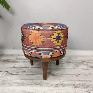 May include: A round, colourful ottoman with a geometric pattern in shades of red, orange, yellow, blue, and black. The ottoman has a wooden base with three legs.