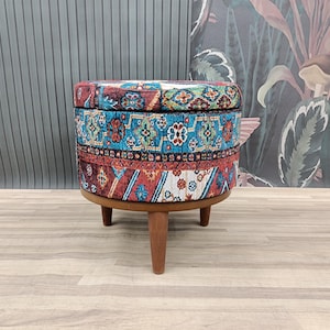 May include: A round, colorful ottoman with a patterned fabric cover and wooden legs. The ottoman has a storage compartment.