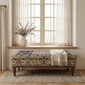 a cozy and inviting living space with a large window, a colorful patterned ottoman, and a vase of greenery on the windowsill.