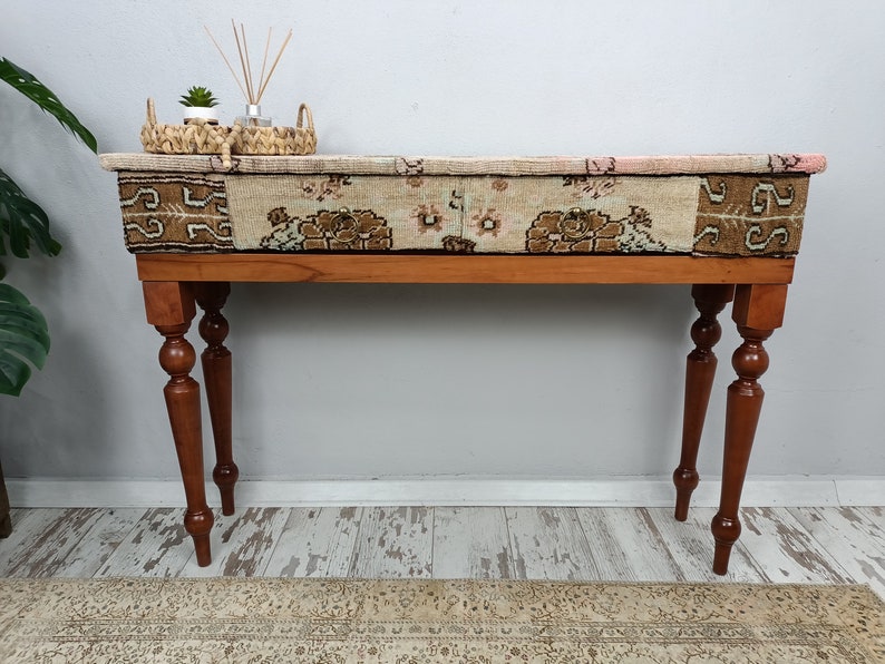 Op de afbeelding: Een houten consoletafel met een blad gemaakt van een patchwork van kleurrijke tapijten. De tafel heeft gedraaide houten poten met decoratieve details.