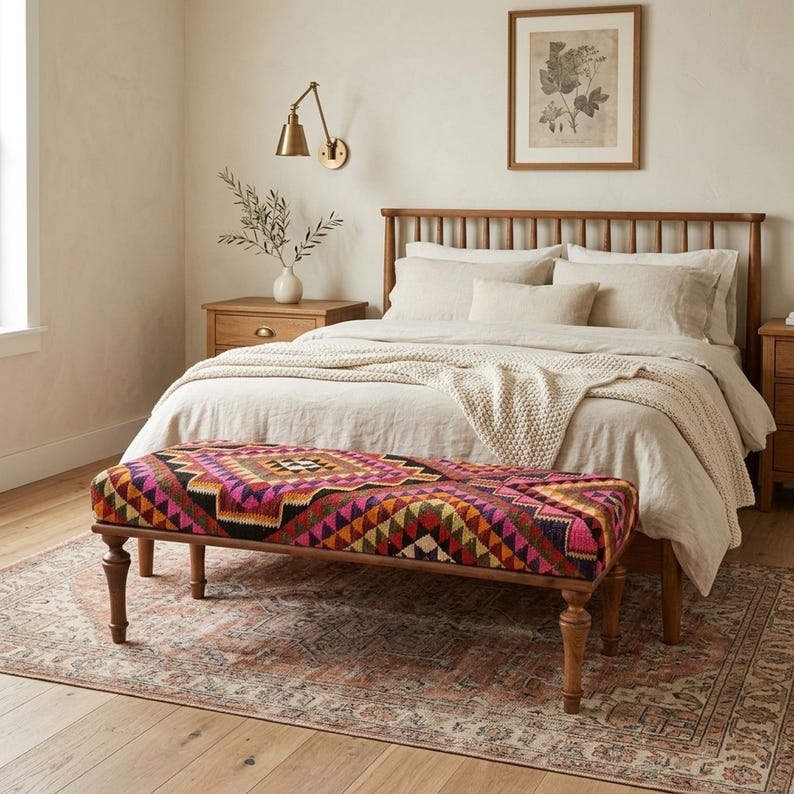a cozy bedroom with a large bed, a wooden headboard, and a colorful patterned bench. The room has a warm and inviting atmosphere, with a rug on the floor and a framed picture on the wall.