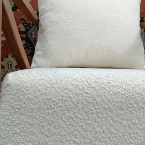 May include: A white chair with a white, textured cushion. The chair has a wooden frame with a geometric pattern.