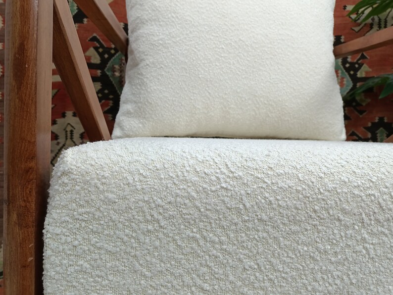 May include: A white chair with a white, textured cushion. The chair has a wooden frame with a geometric pattern.