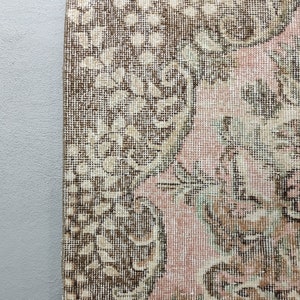 May include: Close-up of a vintage rug with a floral pattern in shades of brown, pink, and cream. The rug has a woven texture and a distressed look.