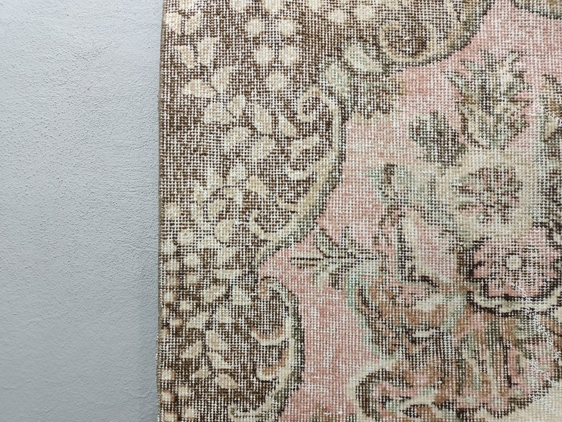 May include: Close-up of a vintage rug with a floral pattern in shades of brown, pink, and cream. The rug has a woven texture and a distressed look.