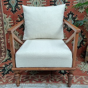 May include: A white armchair with a white cushion and wooden frame. The chair is sitting on a red and black patterned rug.