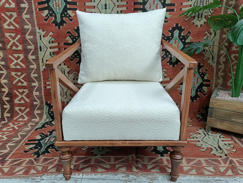 May include: A white armchair with a white cushion and wooden frame. The chair is sitting on a red and black patterned rug.