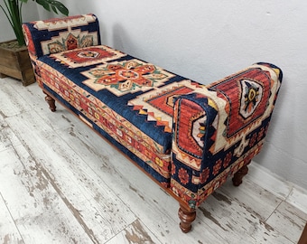 May include: A decorative bench with a patterned design in shades of blue, red, and orange. The bench has a rectangular seat, curved armrests, and four wooden legs. The fabric features a traditional rug-like pattern.