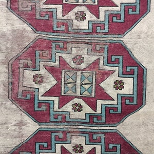 May include: A vintage rug with a repeating pattern of red, blue, and white geometric shapes. The rug has a cream background and a faded appearance.