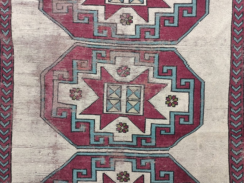 May include: A vintage rug with a repeating pattern of red, blue, and white geometric shapes. The rug has a cream background and a faded appearance.