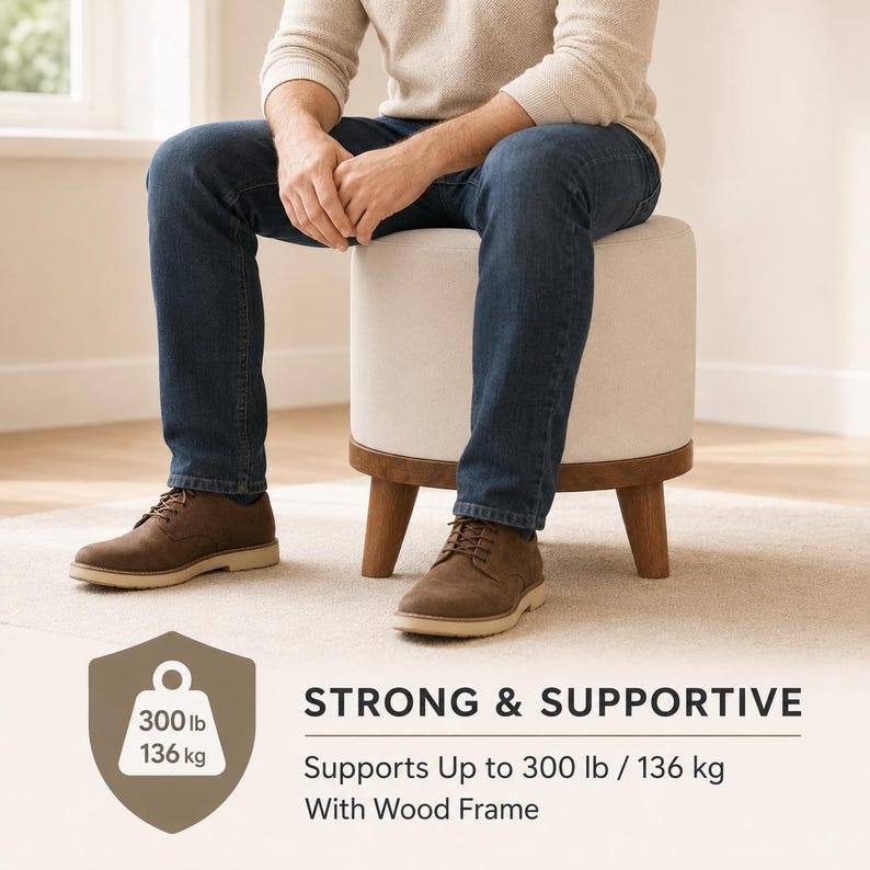 A man sitting on a white ottoman with a wood frame, wearing brown shoes and blue jeans.