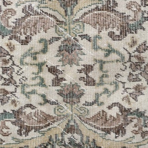 May include: A close-up of a cream-coloured rug with a repeating pattern of brown and green floral designs. The rug is woven with a fine texture and has a subtle sheen.