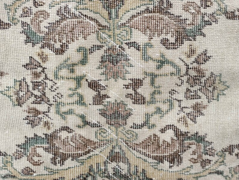 May include: A close-up of a cream-coloured rug with a repeating pattern of brown and green floral designs. The rug is woven with a fine texture and has a subtle sheen.