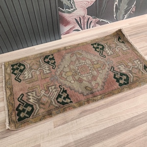 Op de afbeelding: Een roze en groen gestreept tapijt met een traditioneel ontwerp. Het tapijt heeft een gefranst randje en is gemaakt van wol.