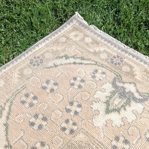 May include: A beige rug with a green and gray floral pattern. The rug has a fringe border.