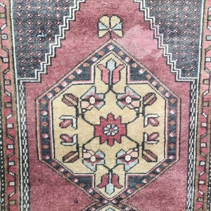 May include: A vintage rug with a traditional Persian design. The rug features a central medallion with floral motifs in shades of beige, red, and blue. The border is a repeating pattern of geometric shapes in black, white, and red.