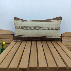 May include: A brown and white striped throw pillow with a woven texture. The pillow is sitting on a wooden bench.
