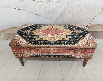 Op de afbeelding: Een rechthoekige opbergottoman met een donkergroene, rode en crèmekleurige stoffen bovenkant. De ottoman heeft vier houten poten.