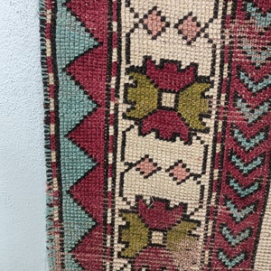 May include: Close-up of a woven rug with a geometric pattern in shades of red, green, blue, and white. The rug has a fringe border.