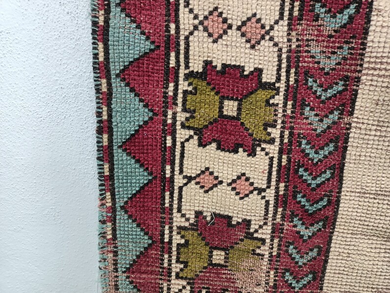 May include: Close-up of a woven rug with a geometric pattern in shades of red, green, blue, and white. The rug has a fringe border.
