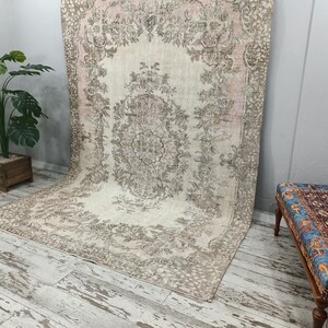 May include: A vintage rug with a floral pattern in shades of beige, pink, and brown. The rug is laid out on a whitewashed wood floor.