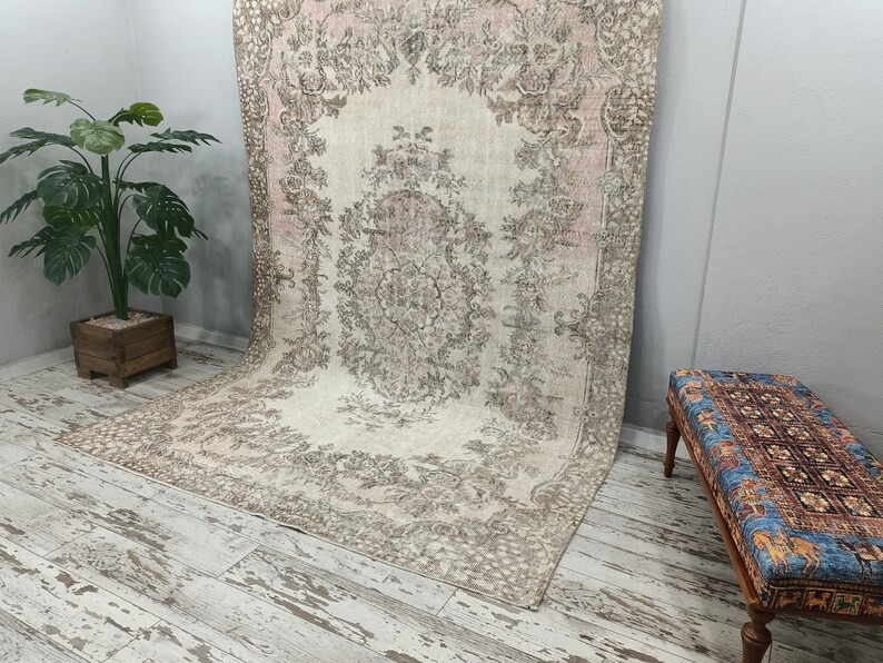 May include: A vintage rug with a floral pattern in shades of beige, pink, and brown. The rug is laid out on a whitewashed wood floor.