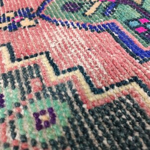 Peut inclure: Gros plan sur un tapis tiss&eacute; color&eacute; avec un motif g&eacute;om&eacute;trique. Le tapis est en laine et a une surface douce et textur&eacute;e.