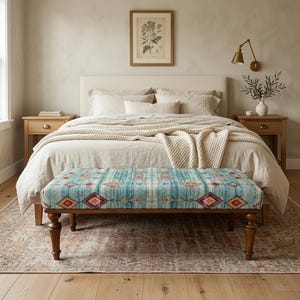 May include: A bedroom scene featuring a bed with neutral-colored bedding, a patterned bench at the foot, and two wooden nightstands. The bench has a blue, teal, and red geometric design. A framed botanical print hangs above the bed.
